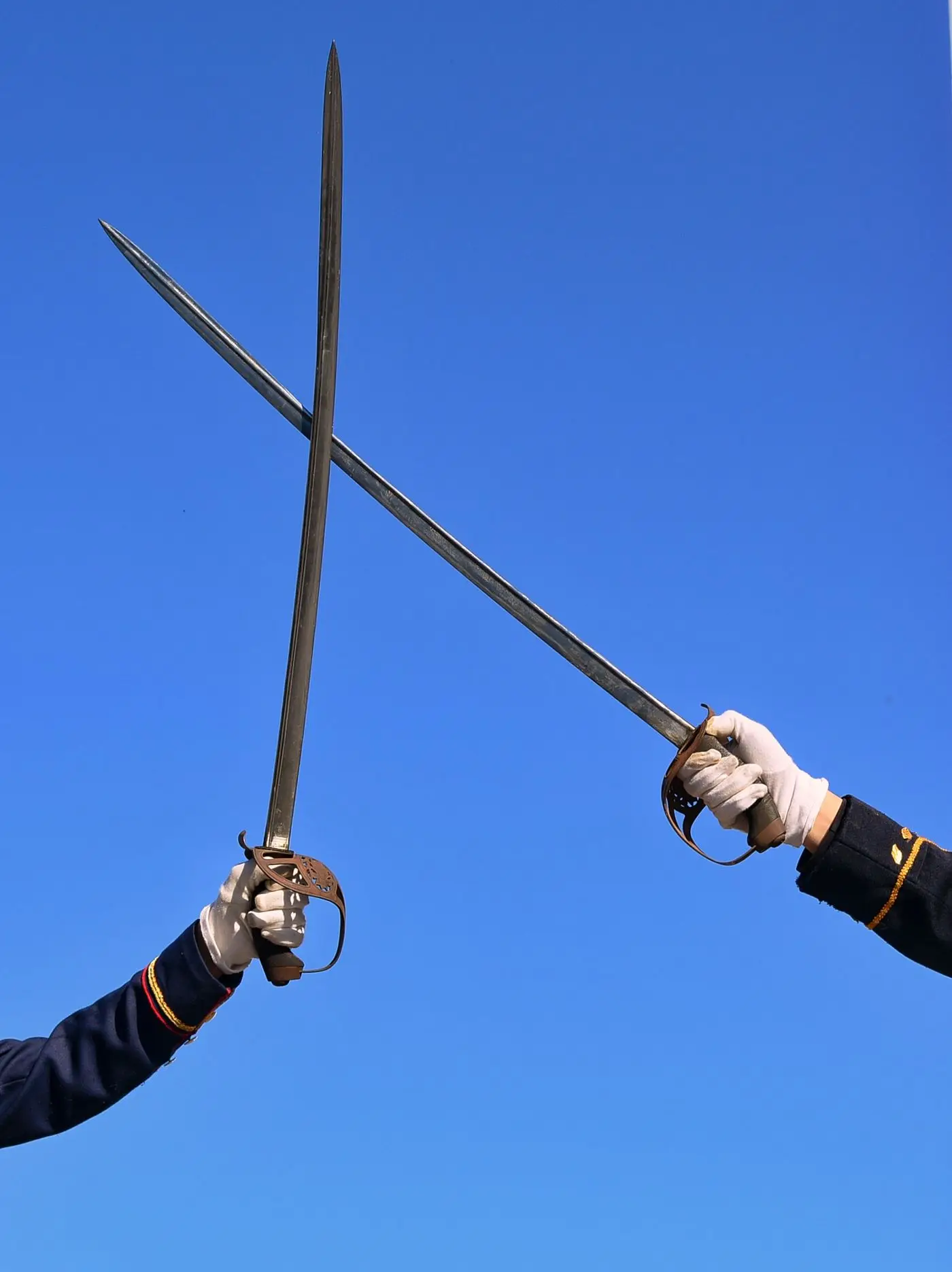 Two gloved hands crossing sabres against a plain sky